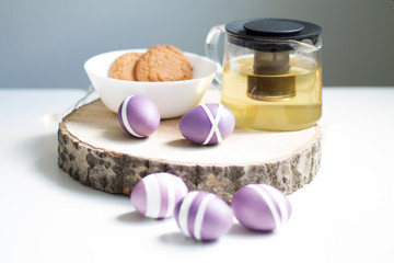 lilac Easter eggs on wooden stand with tea and cookies
