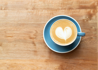 Top view of hot Coffee cup with a barista art heart shape foam on wooden table background with copy text space.