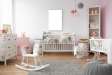 White rocking horse on grey rug in child's bedroom interior with mockup on empty poster. Real photo