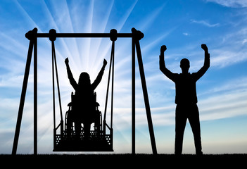 Silhouette of a happy couple, a woman wheelchair user on an adaptive swing and a healthy man nearby.