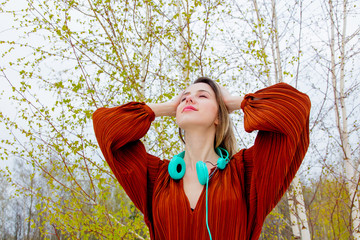 Style adult woman with headphones and burgundy color blouse on birch trees background