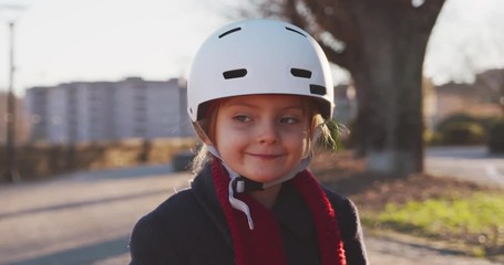 happy smiling daughter child girl wearing safety helmet riding bicycle portrait at city park.Childhood,active,safety concepts.Sidewalk urban outdoor.Warm sunset backlight.4k slow motion video