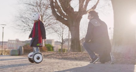 Daughter child girl learning segway riding with dad teaching in city.Modern future transport technology.Active safety family.Sidewalk urban outdoor.Warm sunset cold backlight.4k slow motion 60p video