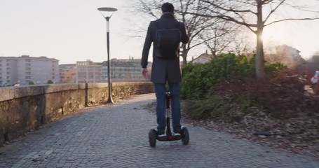 Business man riding segway in city commuting to work or home while calling using smartphone.Modern future transport technology.Sidewalk urban outdoor.Warm sunset backlight.4k slow motion 60p video