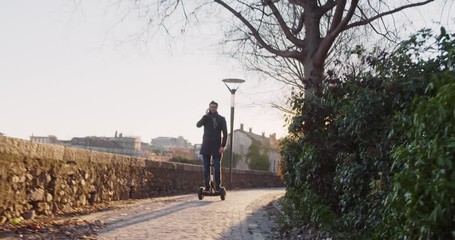 Business man riding segway in city commuting to work or home while calling using smartphone.Modern future transport technology.Sidewalk urban outdoor.Warm sunset backlight.4k slow motion 60p video