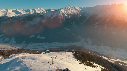 Aerial helicopter shot of calm rural mountain landscape, snow-covered mountain peaks and ski resort landscape at the Austrian Alps on a sunny afternoon day