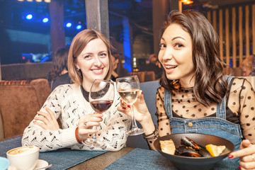 Two girl friends have fun and chat while drinking a glass of wine in a restaurant in a nightclub. The concept of relaxing and frienship