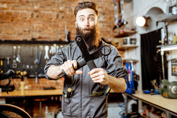 Portrait of a handsome bearded repairman in workwear standing with wrenches at the bicycle workshop