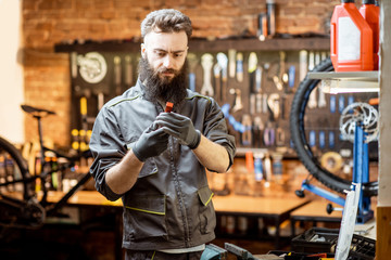 Handsome bearded repairman in workwear working in the beautiful bicycle workshop
