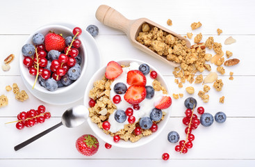 Breakfast with yogurt, muesli and berries on white wood background, top view