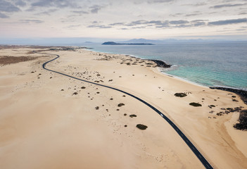 Car on the empty road, through the sand dunes, at Corralejo Natural Park before the sunset with copy space