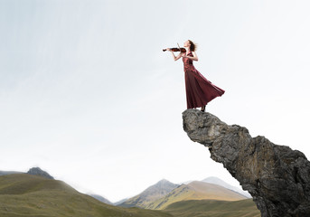 Woman violinist in red dress playing melody against cloudy sky