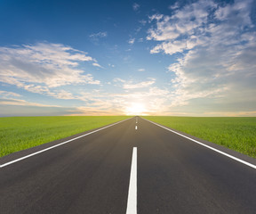 asphalt road among a green fields at the sunset, natural road background