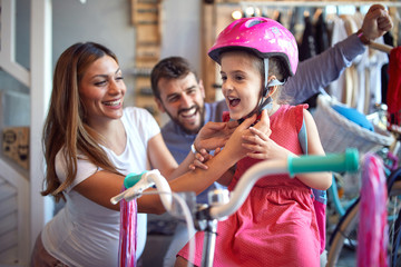 Sale, consumerism and people concept - woman choosing new bicycle and helmet for little girl in bike shop .