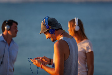 Three people in headphones, spending time in the open air nearby the sea