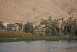 Nile River, Egypt: Two men in a rowboat, farmers with their cattle, date palm trees, houses, and sand dunes along the west bank of the Nile River.