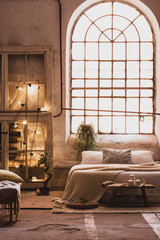 Lights on wooden cabinet in bright loft bedroom interior with window above bed with pillows. Real photo
