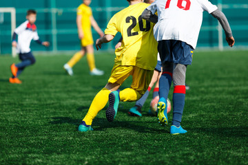 Boys at white yellow sportswear run, dribble, attack on football field. Young Soccer players with ball on green grass. Training, football, active lifestyle for kids  