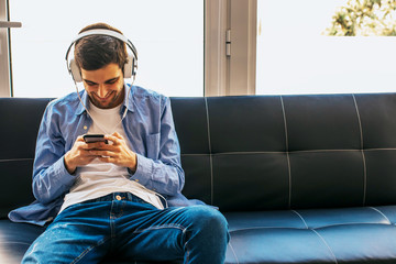 young man or teenager with mobile phone and headphones at home