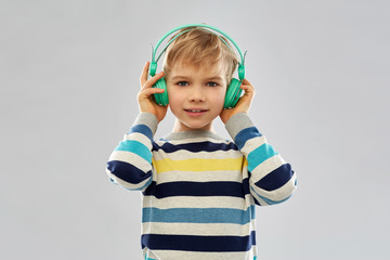 technology, audio equipment and people concept - portrait of smiling little boy in headphones in striped pullover listening to music over grey background