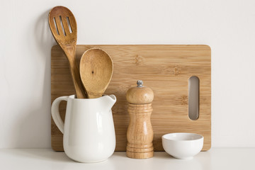 Kitchenware cutting board, spoons and spice mill on table wall background