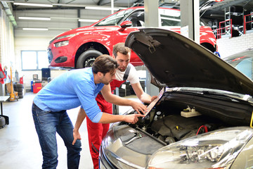 after-sales service in the car repair shop - mechanic and man talk about repairing a vehicle