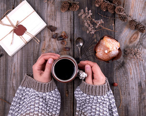 women's hands in a knitted brown sweater holding a ceramic mug with black coffee