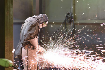 Industriearbeiter arbeitet mit einer Schleifmaschine/ Flex - Bearbeitung Werkstück aus Metall in einer Giesserei // Industrial worker works with a grinding machine/ flex - machining metal workpiece in