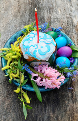 Easter cake with a candle, painted eggs, spring branches and flowers. Easter composition on the old wooden table.