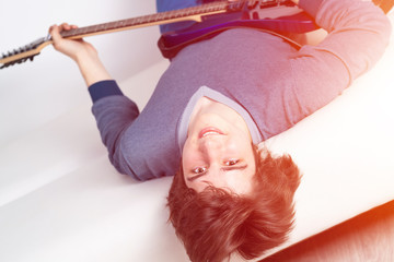 Happy young man lying back on sofa with guitar