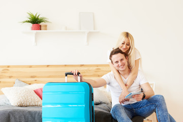 Smiling couple of tourists with passports and tickets in hotel room keep a suitcase with luggage. Waiting for a flight from the airport. The girl hugs the guy, they are going on a honeymoon trip