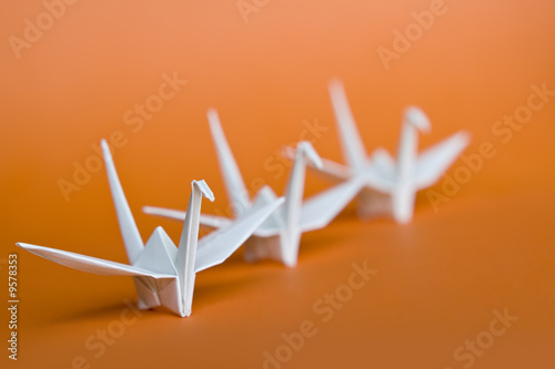 trzy-biale-ptaki-origami-w-kolejce-na-pomaranczowym-tle