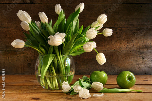 Fototapeta White tulips in glass vase on rustic wood