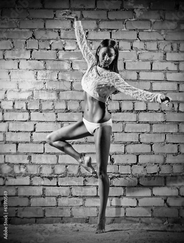 Fototapeta Young dancing woman on brick wall (monochrome version)
