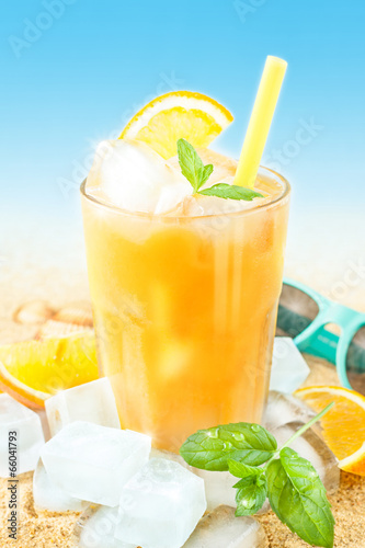  Cold orange juice with ice on beach background