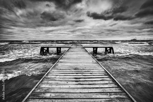 Old wooden jetty during storm on the sea. Dramatic sky