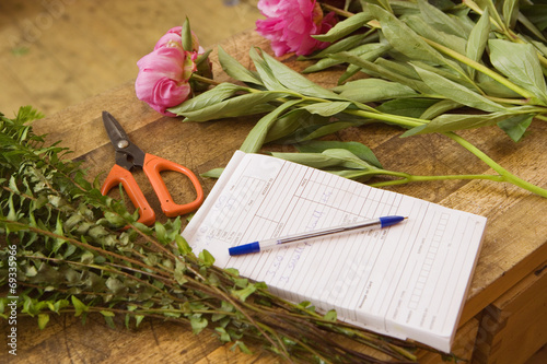 Pink flowers on table beside order pad and scissors in flower shop, close-up (still life)
