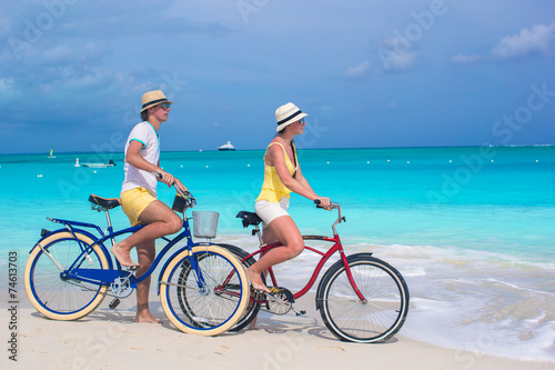 Young happy couple riding bikes on white tropical beach