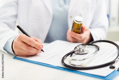 Zdjęcia Female doctor filling medical form holding medicine bottle