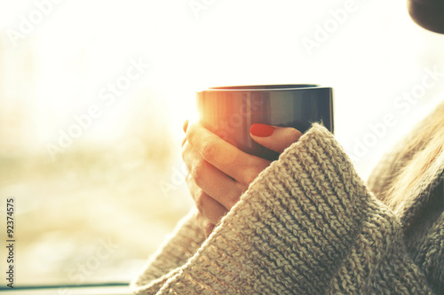 hands holding hot cup of coffee or tea in morning sunlight