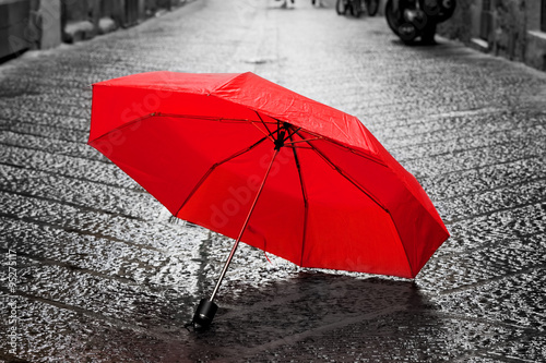  Red umbrella on cobblestone street in the old town. Wind and rain