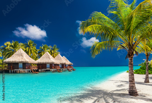 Fotografiet Over water bungalows on a tropical island with palm trees and am