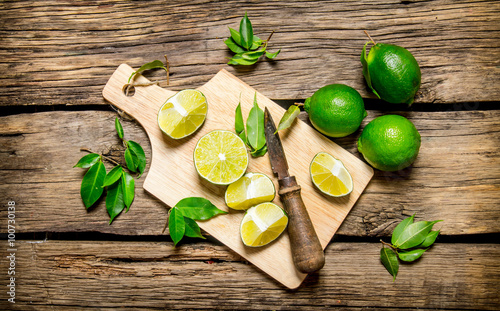 Sliced limes on a wooden board with leaves and knife.