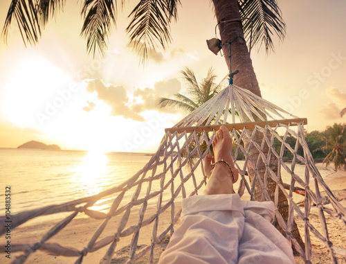 Female legs in a hammock on a background of the sea, palm trees and sunset. Vacation concept
