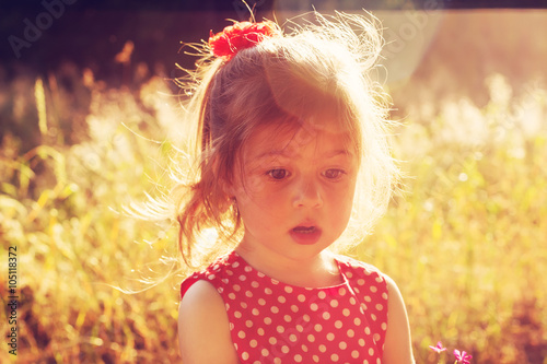 Sad Little girl walking on meadow at summer sunset