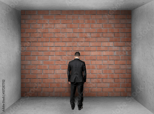 Poster Businessman with bowed head stands front of a brick wall in interior