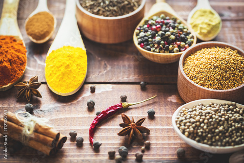 Beautiful colorful spices in wooden spoons and bowls on an old wooden brown table Poster