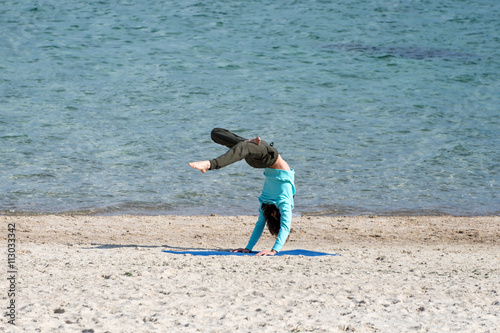 Poster Man doing yoga on the seashore. Young exercising at the beach.