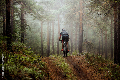 male athlete mountainbiker rides a bicycle along a forest trail. in forest mist, mysterious view