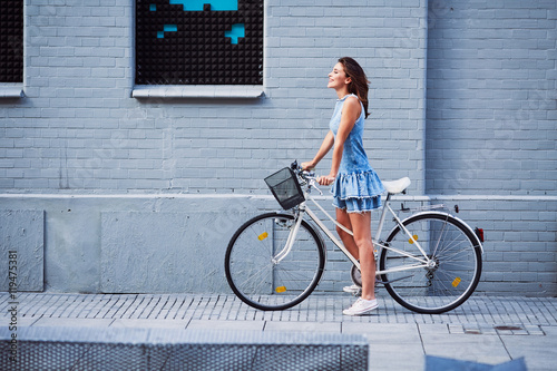 Happy woman with bike standing agains brick building